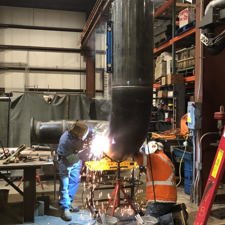 Two workers welding a pipe. NBW Inc.