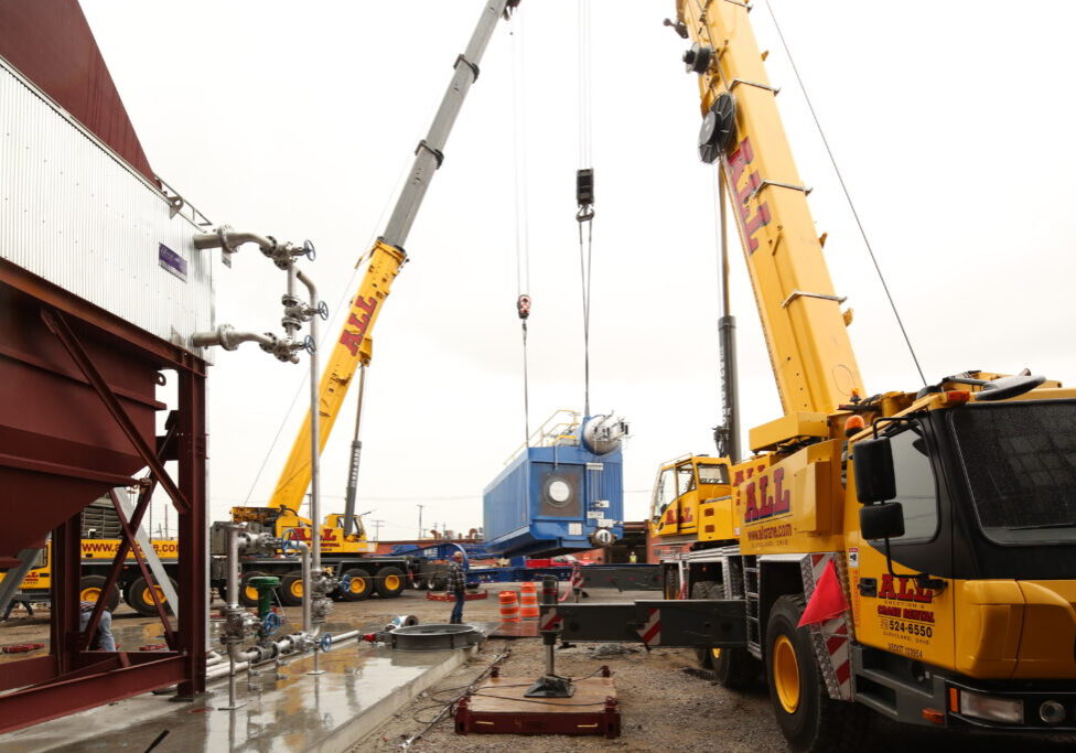 Two yellow cranes lifting a blue boiler unit. NBW Inc.