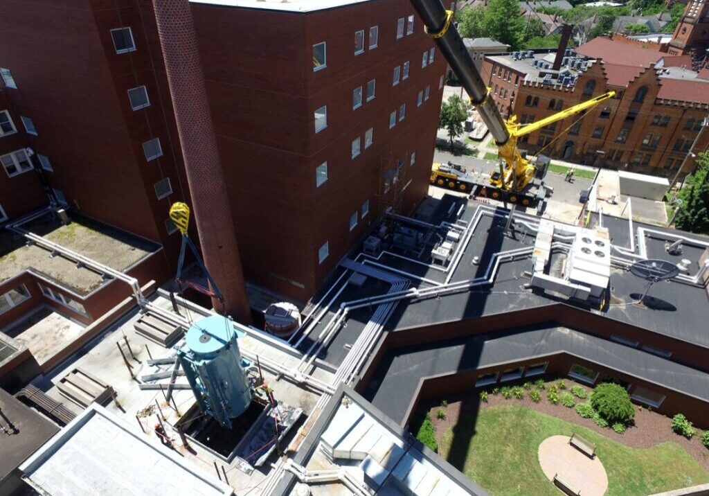 Aerial photo of a crane lifting a boiler into a building. The National Board of Boiler & Pressure Vessel Inspectors Certificate of Authorization. NBW Inc.